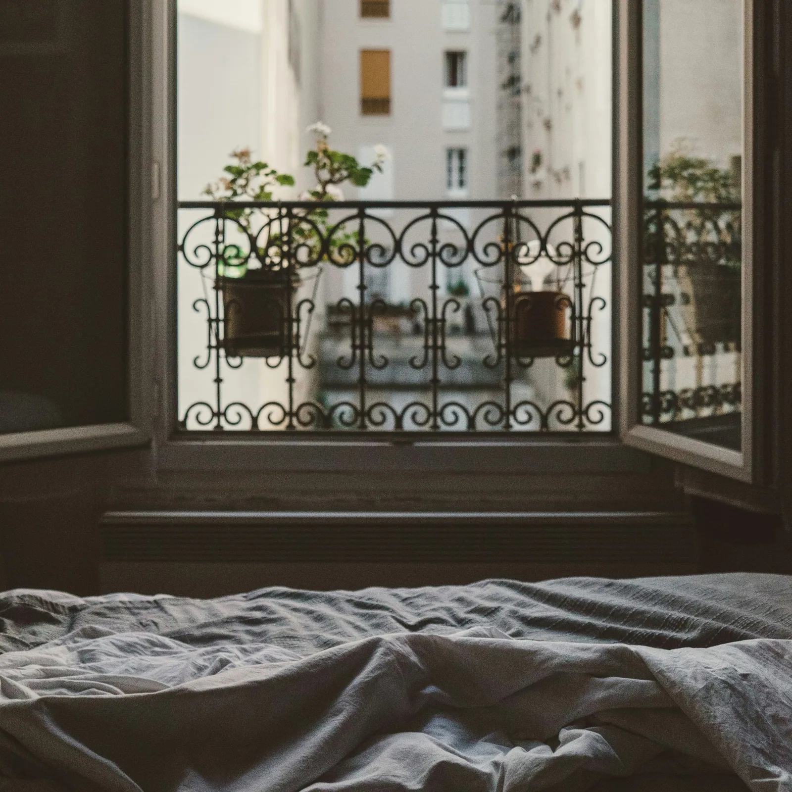 A softly made bed beside a window in low evening light