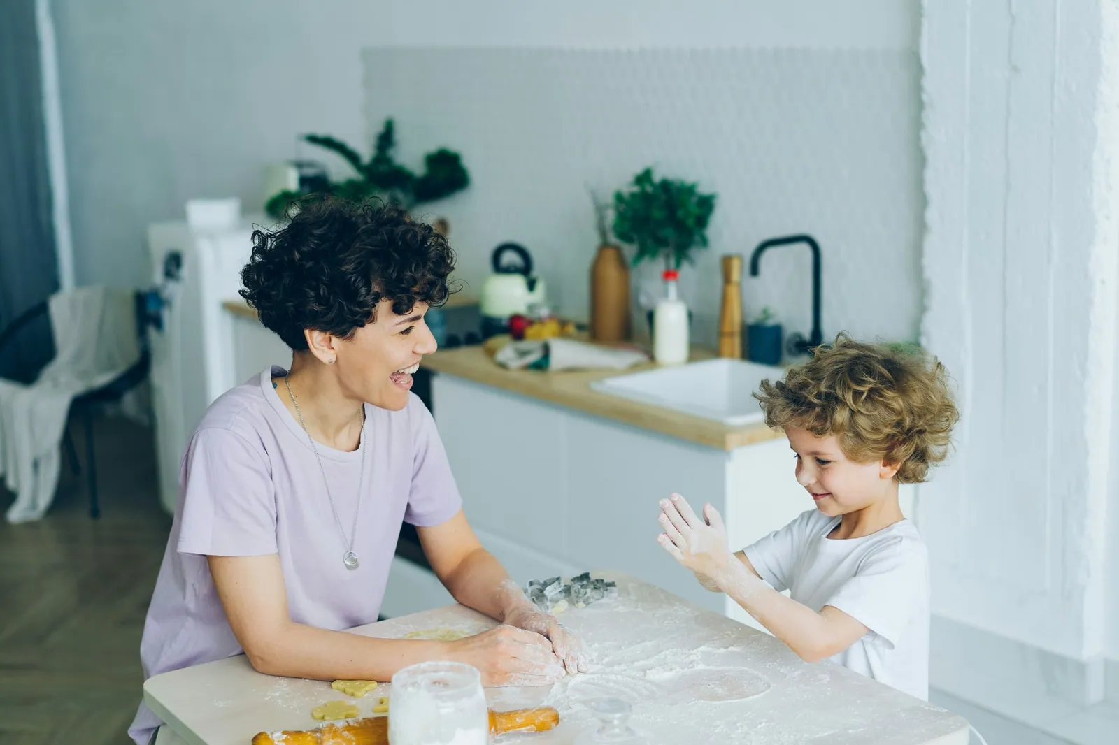 A parent and child baking together at a kitchen table, flour on their hands