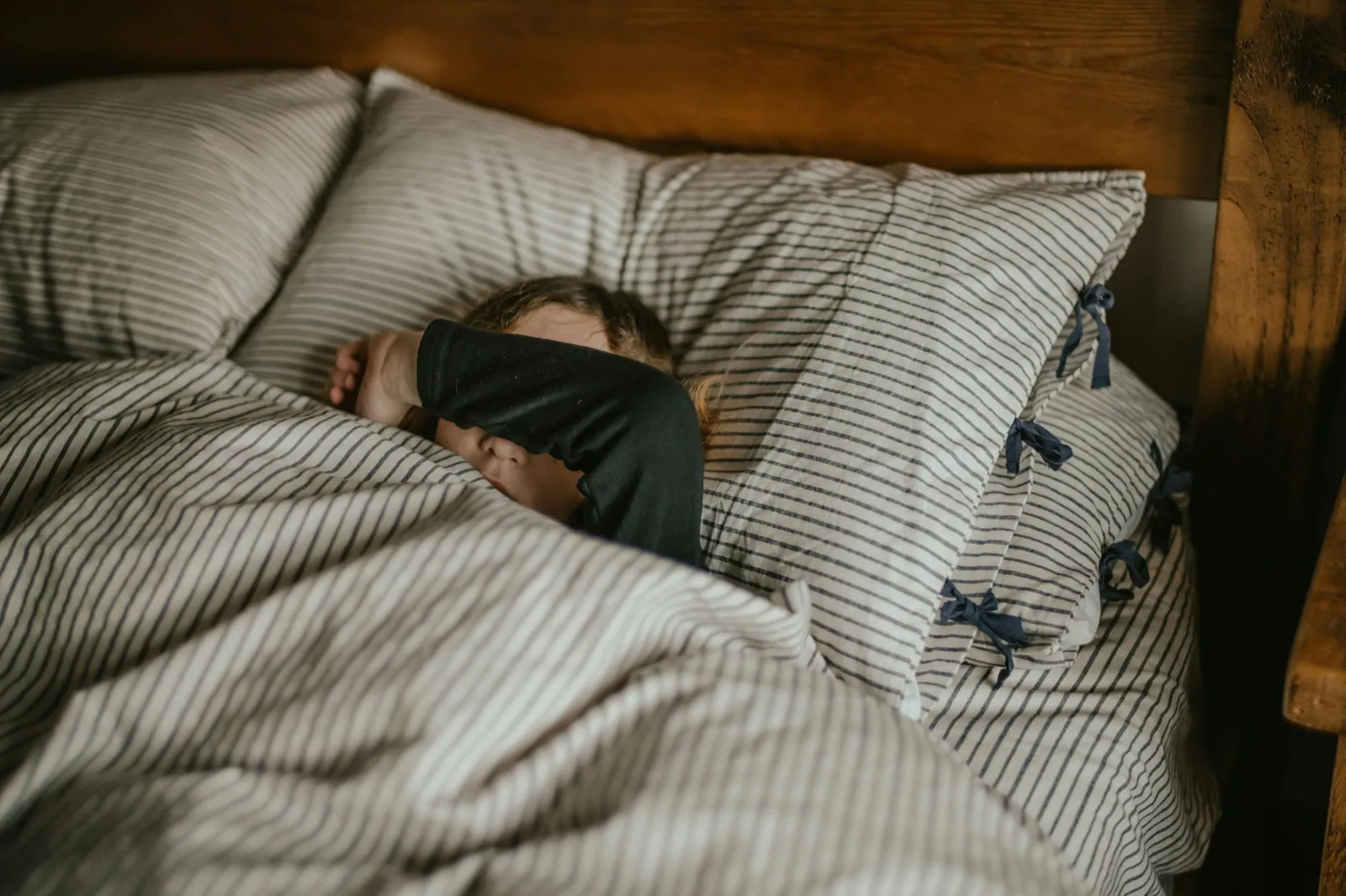 A teenager asleep in a rumpled bed in the early morning, eye mask on, curtains still drawn