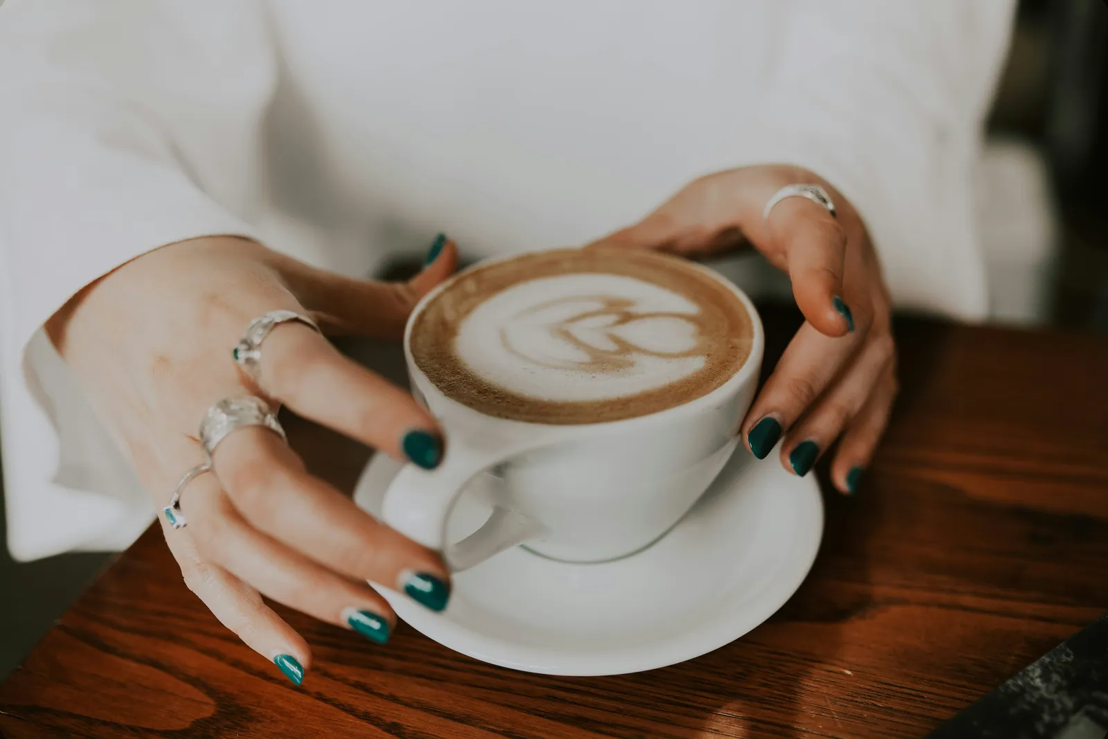 A woman's hands wrapped around a coffee cup at a wooden table, taking a moment