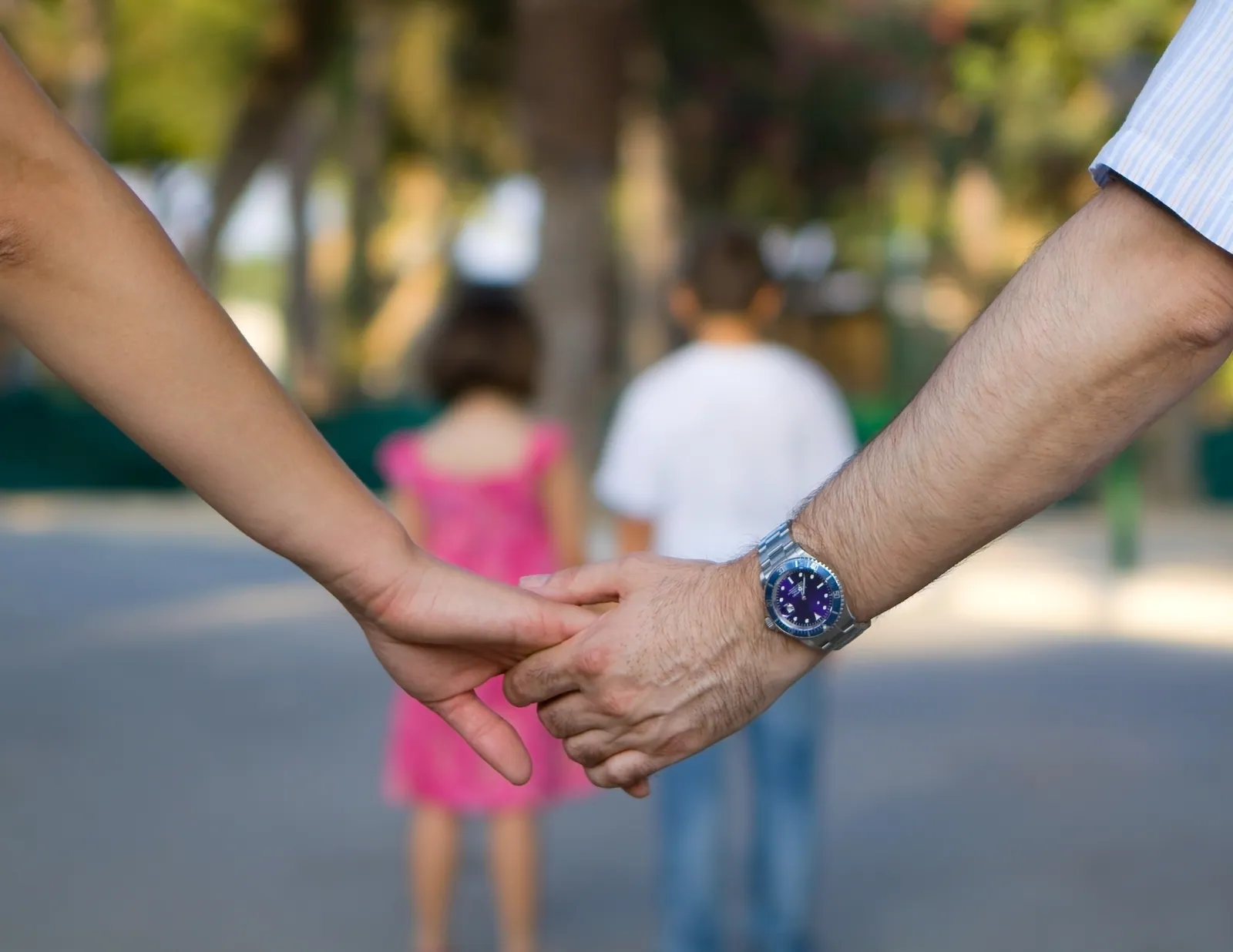 Two parents holding hands while their child walks ahead, reflecting a shared approach to family life