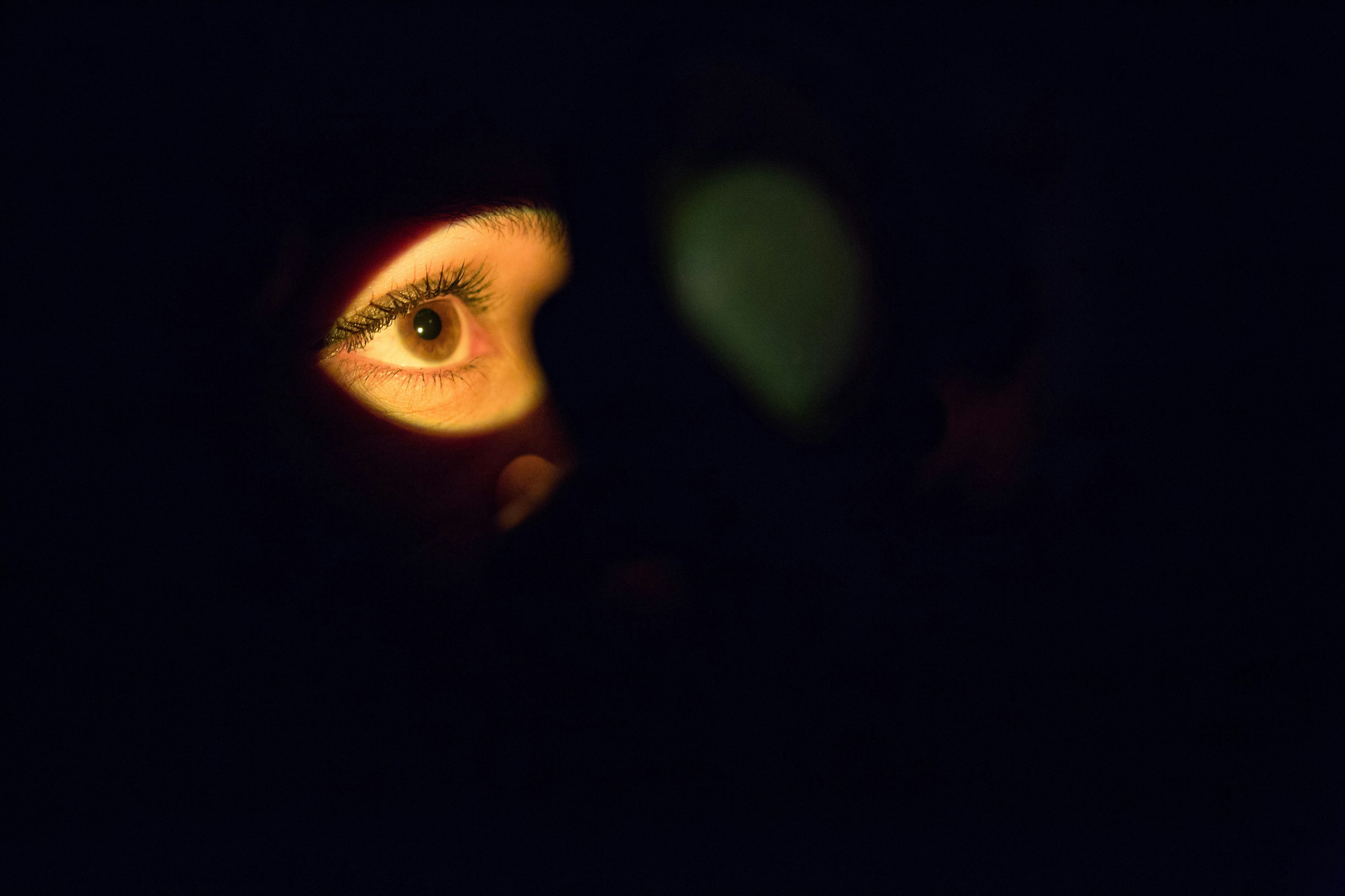 A single eye lit by the glow of a screen in an otherwise dark room