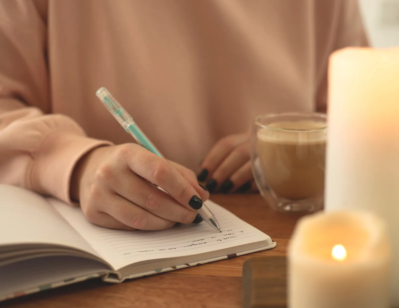 A person writing in a notebook by candlelight, a warm mug nearby, in soft golden morning light