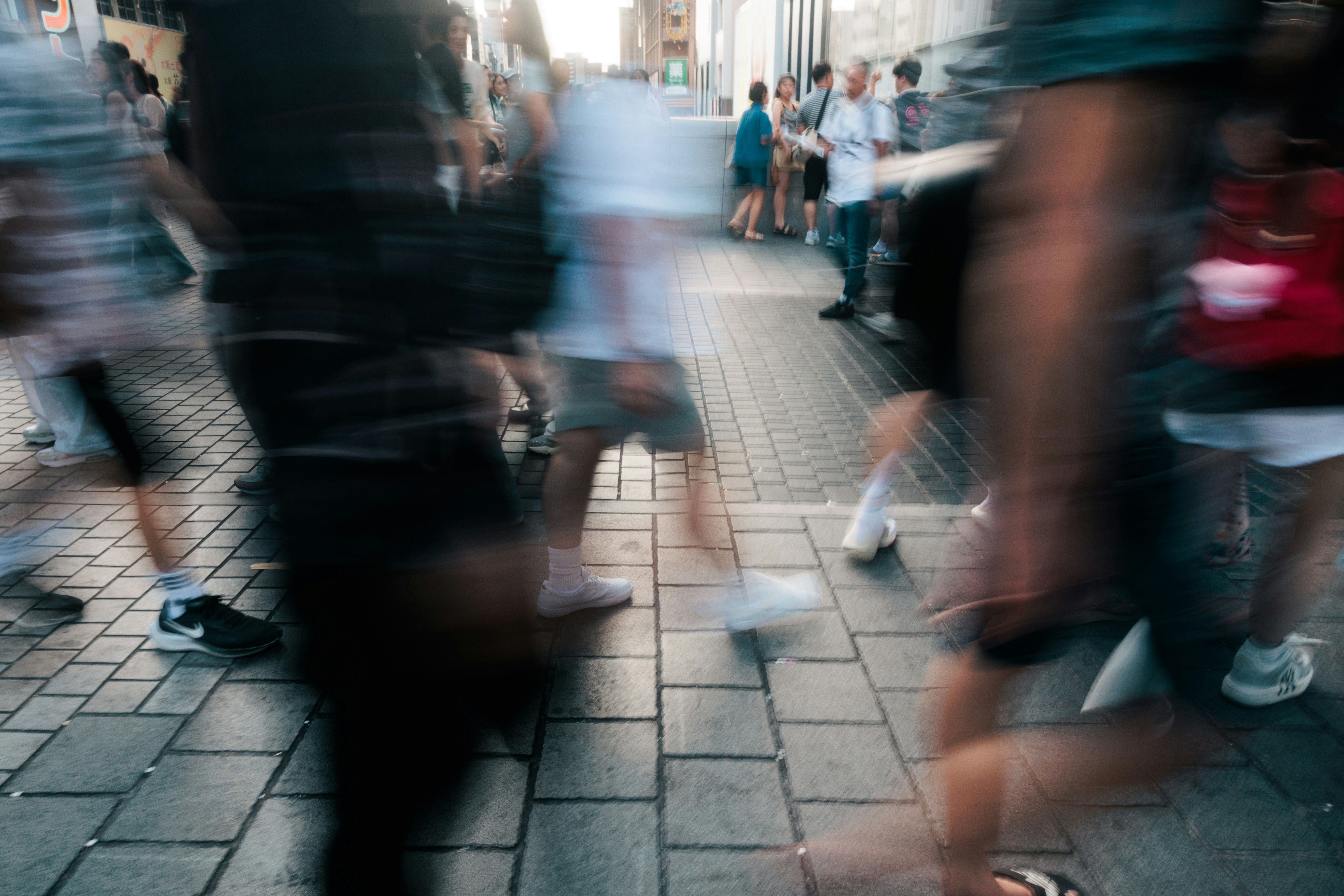A busy pavement where everyone is blurred with motion and one figure stands still