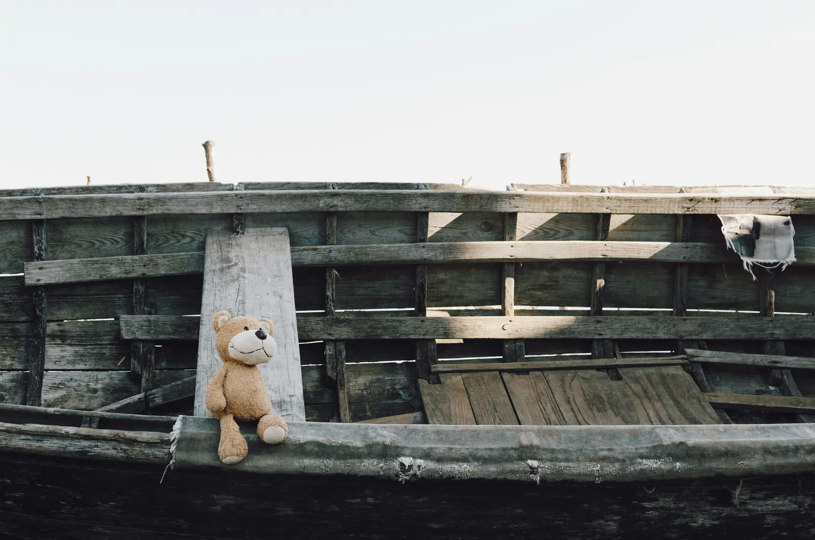 A small teddy bear sitting alone at the end of a wooden boat on still water