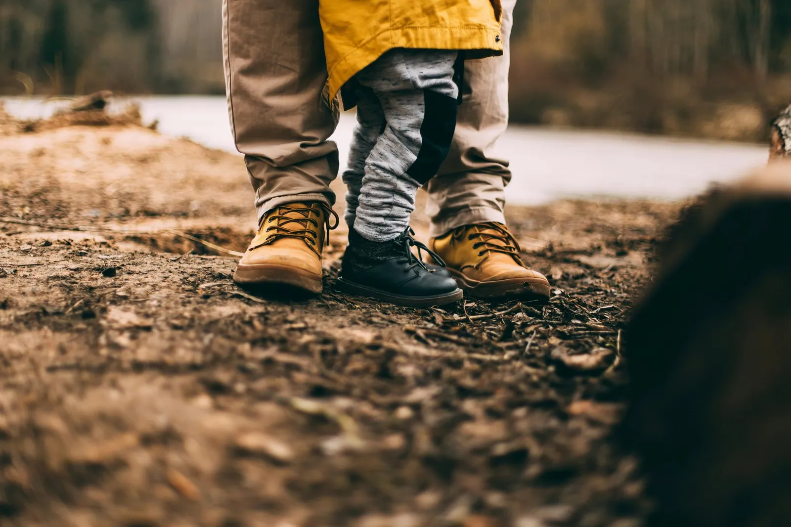 A small child standing on their parent's boots on a woodland path