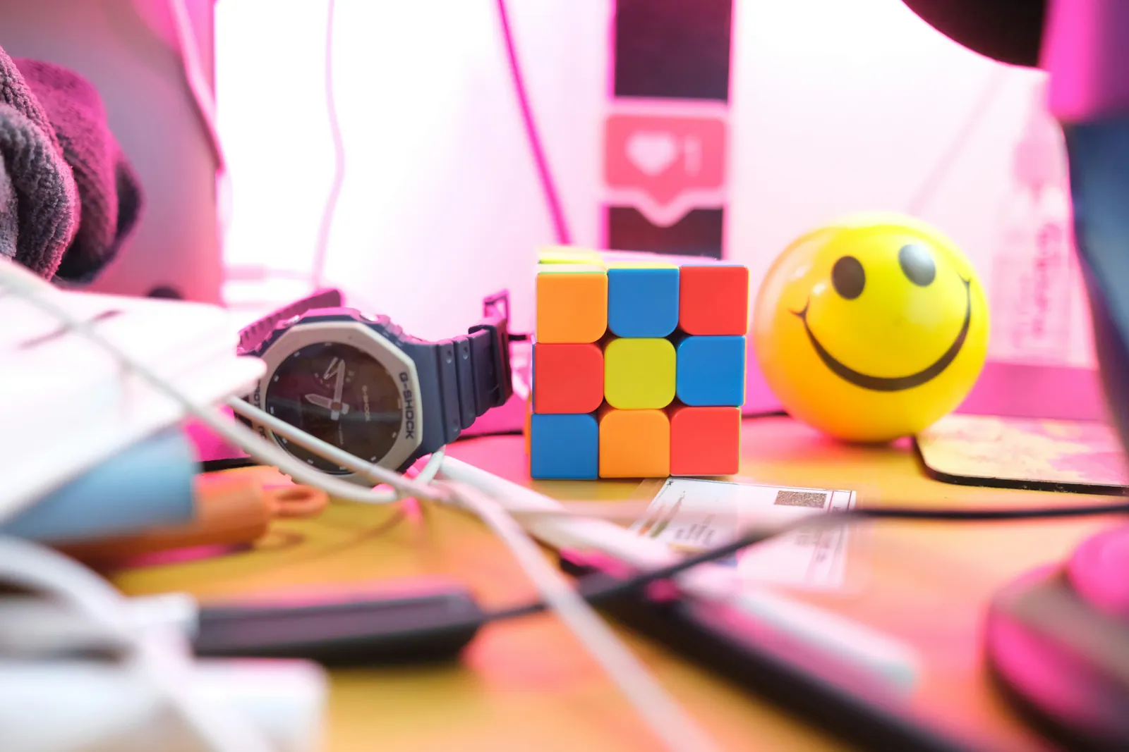 A desk with a watch, a Rubik cube, a smiley clock and tangled charging cables