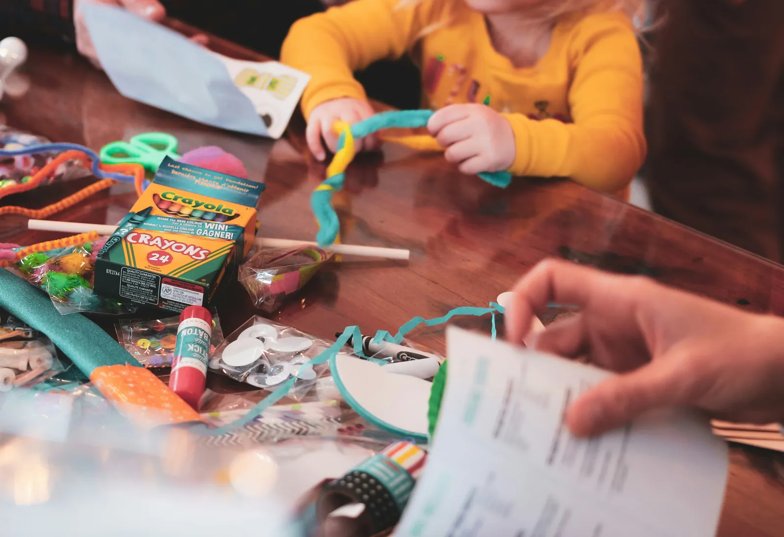 A child at a table covered in craft supplies, paper scraps, glue and scattered pens