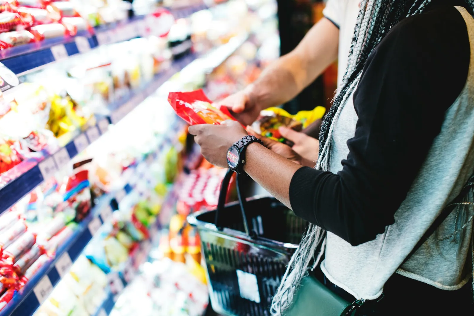 A parent with a shopping basket reaching along a busy supermarket aisle