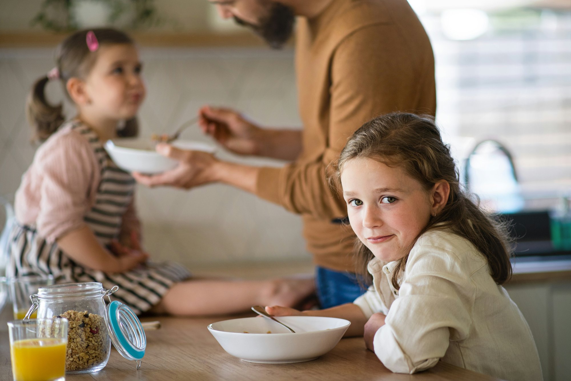 A family eating breakfast together in a bright kitchen, a girl looking towards the camera