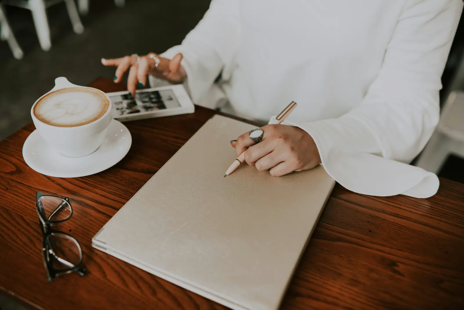 A notebook, pen and cup of coffee on a wooden table with glasses set to one side