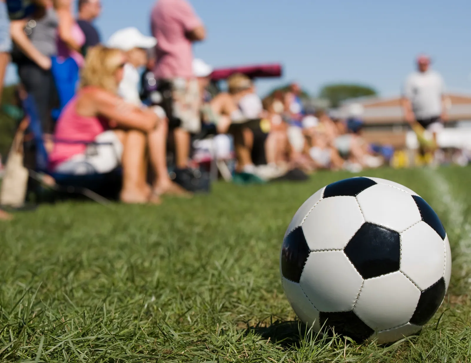A football on the grass while families share time together on the sideline during a relaxed weekend