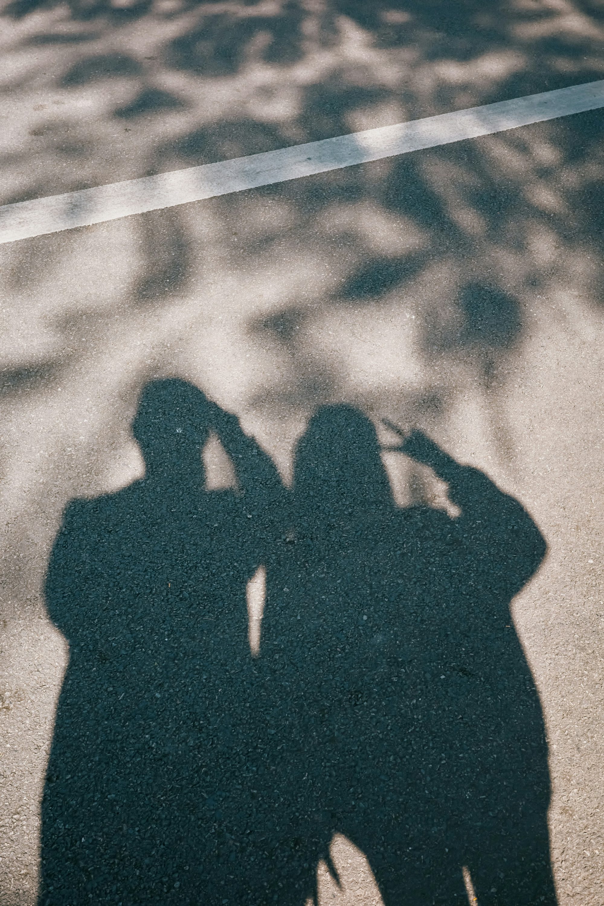 The shadows of two people standing together on sunlit pavement