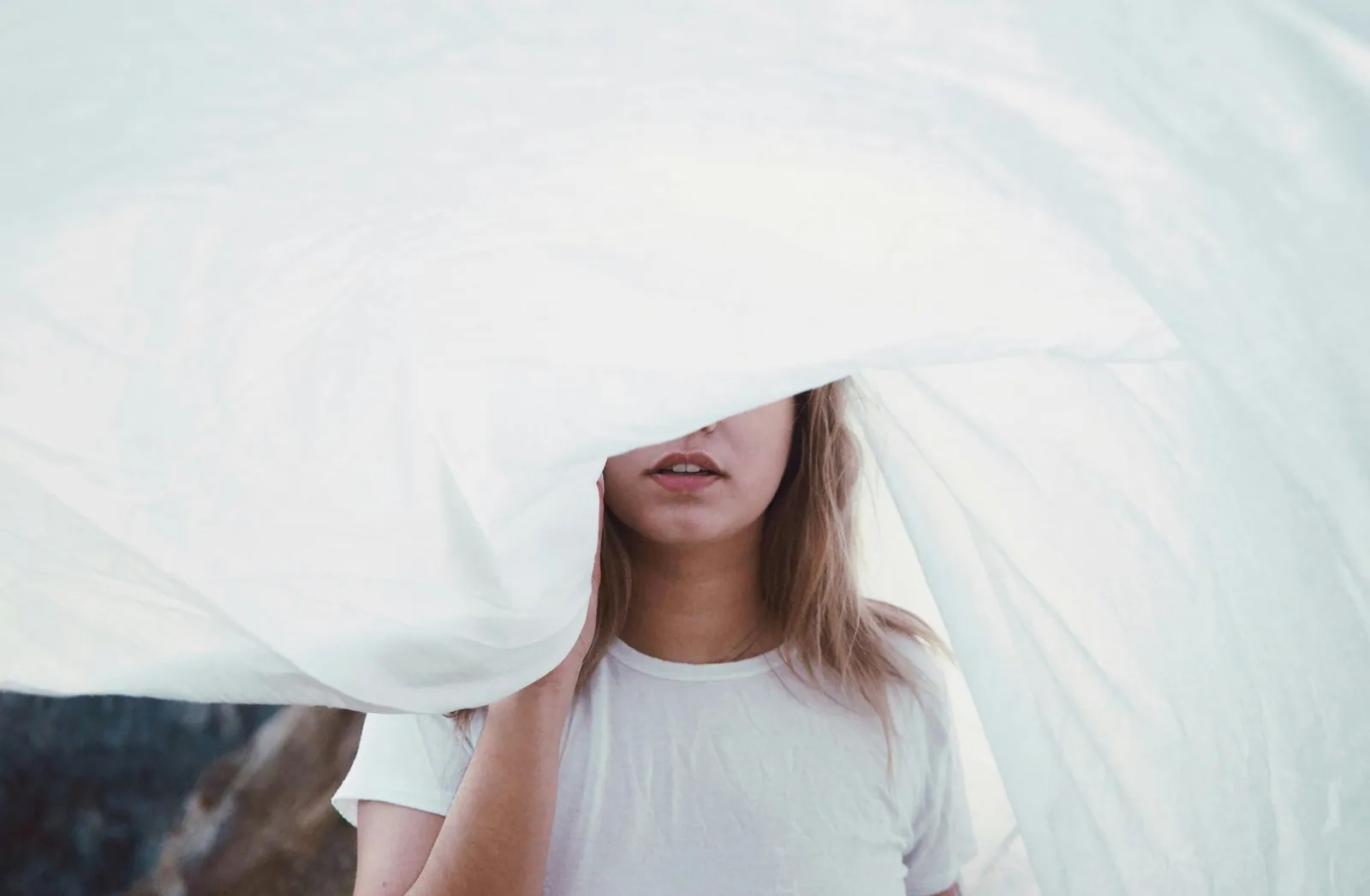 A child peeking out from under a white duvet pulled over their head