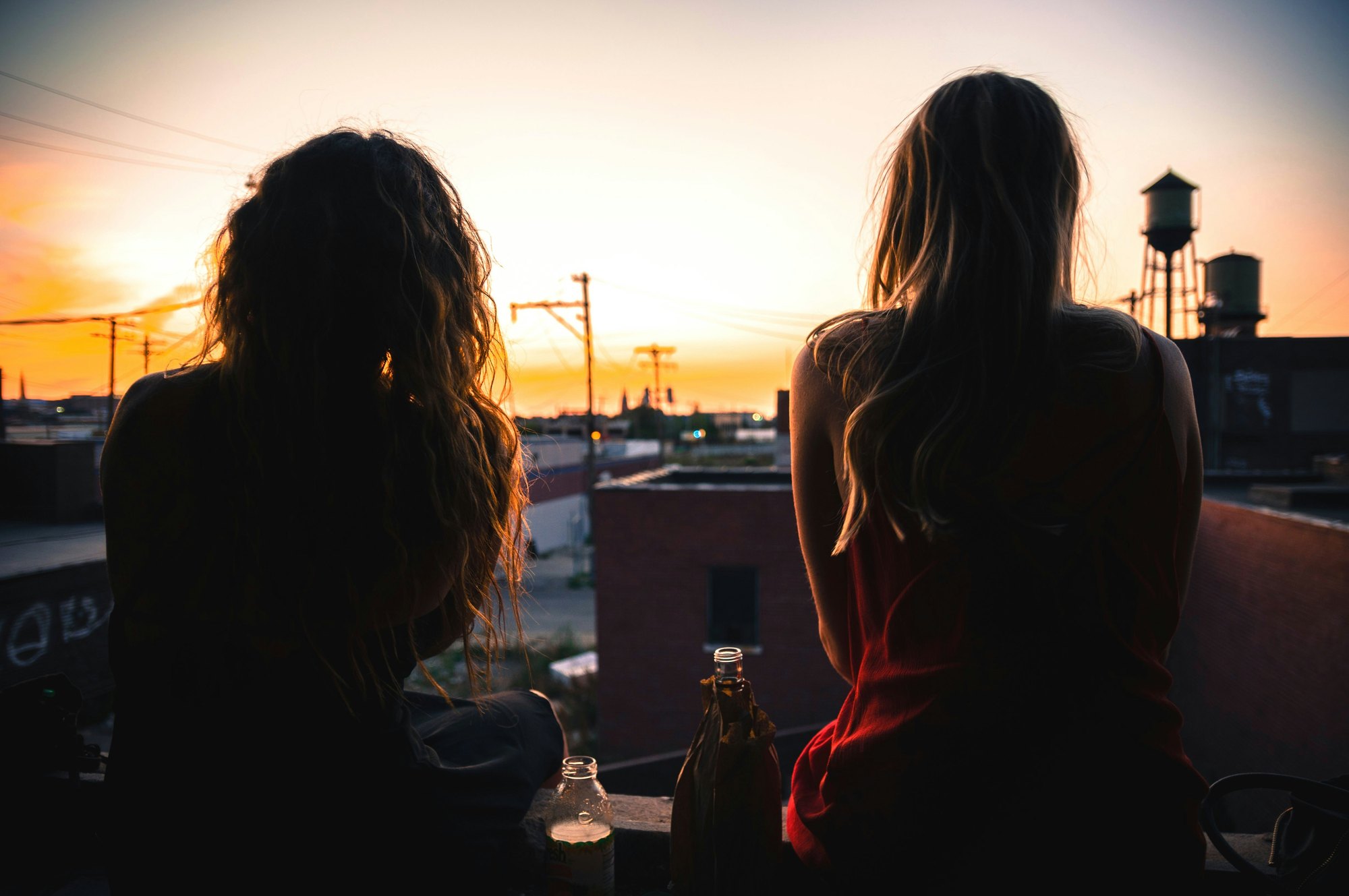 Two teenagers sitting together watching the sun go down over the rooftops