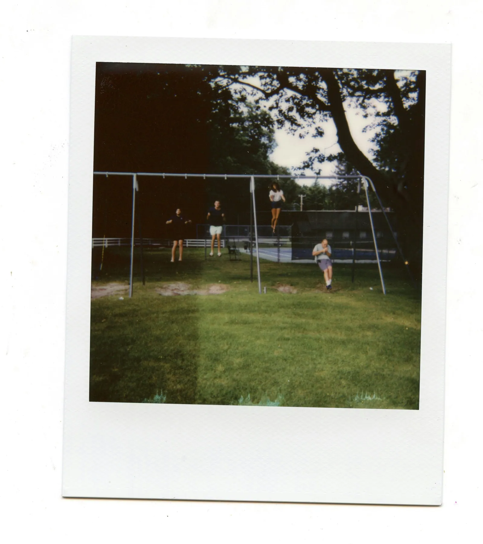 A polaroid photograph of an empty set of swings in a summer garden