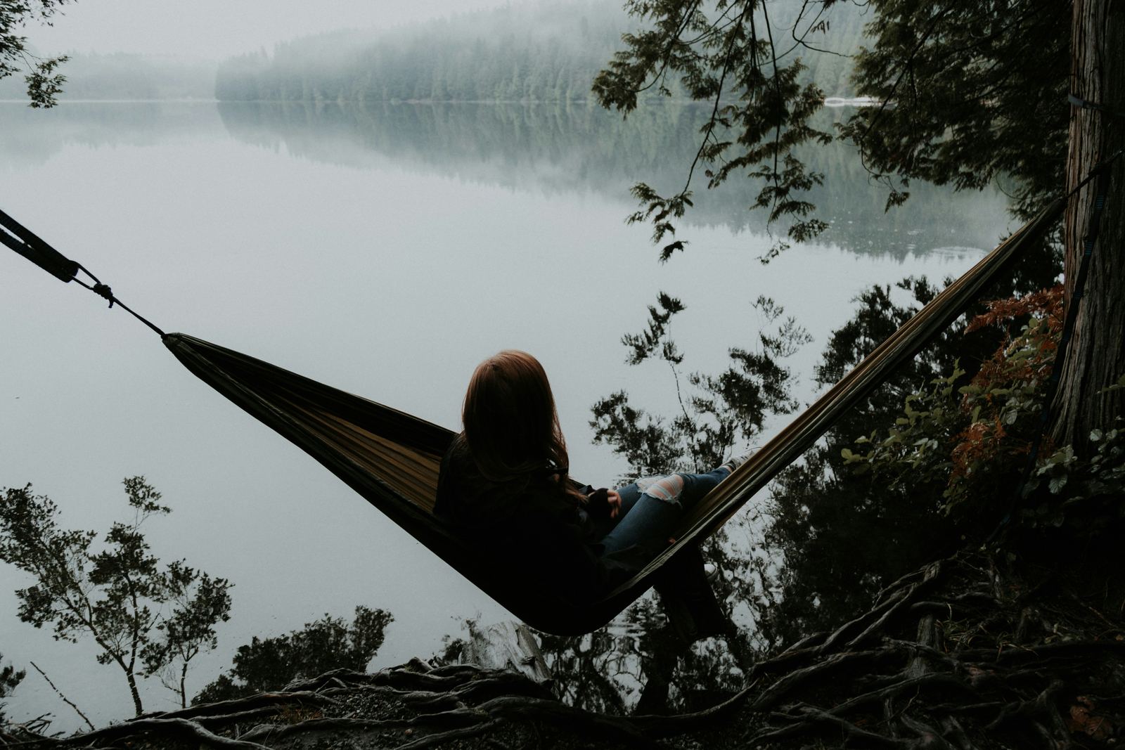 A person resting alone in a hammock beside a still lake