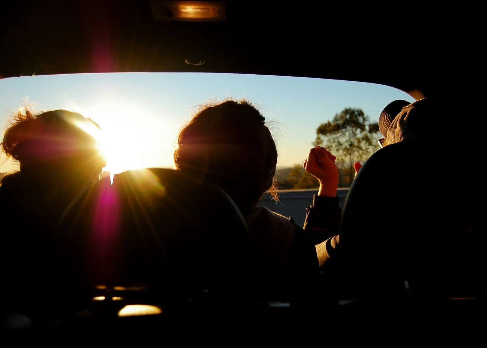 Teenagers in a car at sunset, seen in silhouette through the windscreen