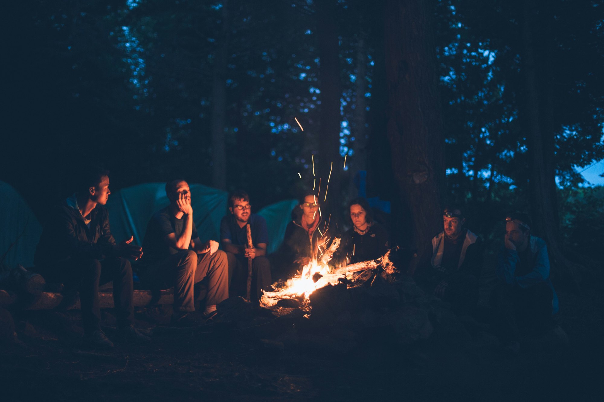 Young people gathered around a campfire in the woods at night