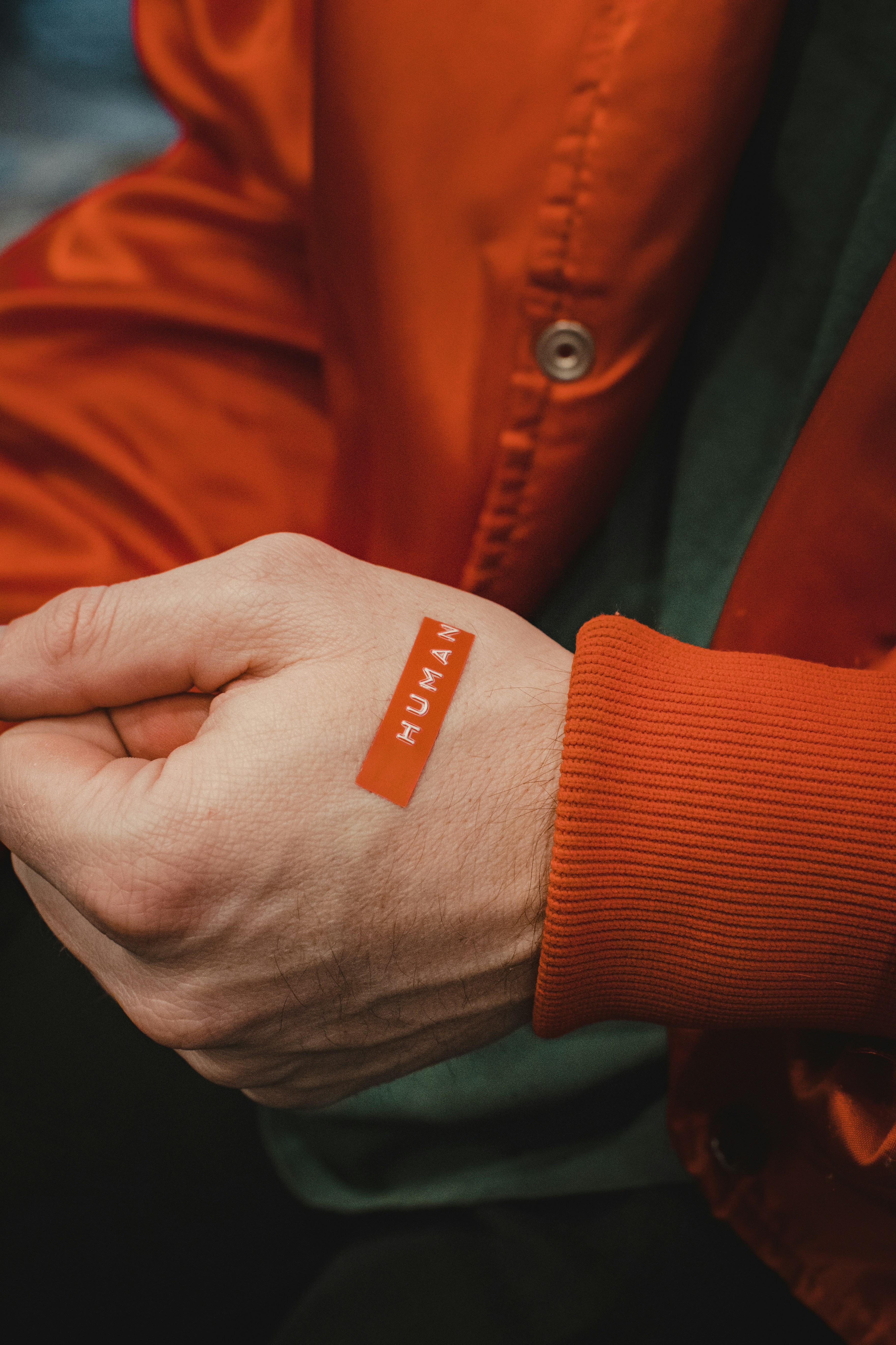 A hand with a plaster across the knuckle, held against a bright orange sleeve