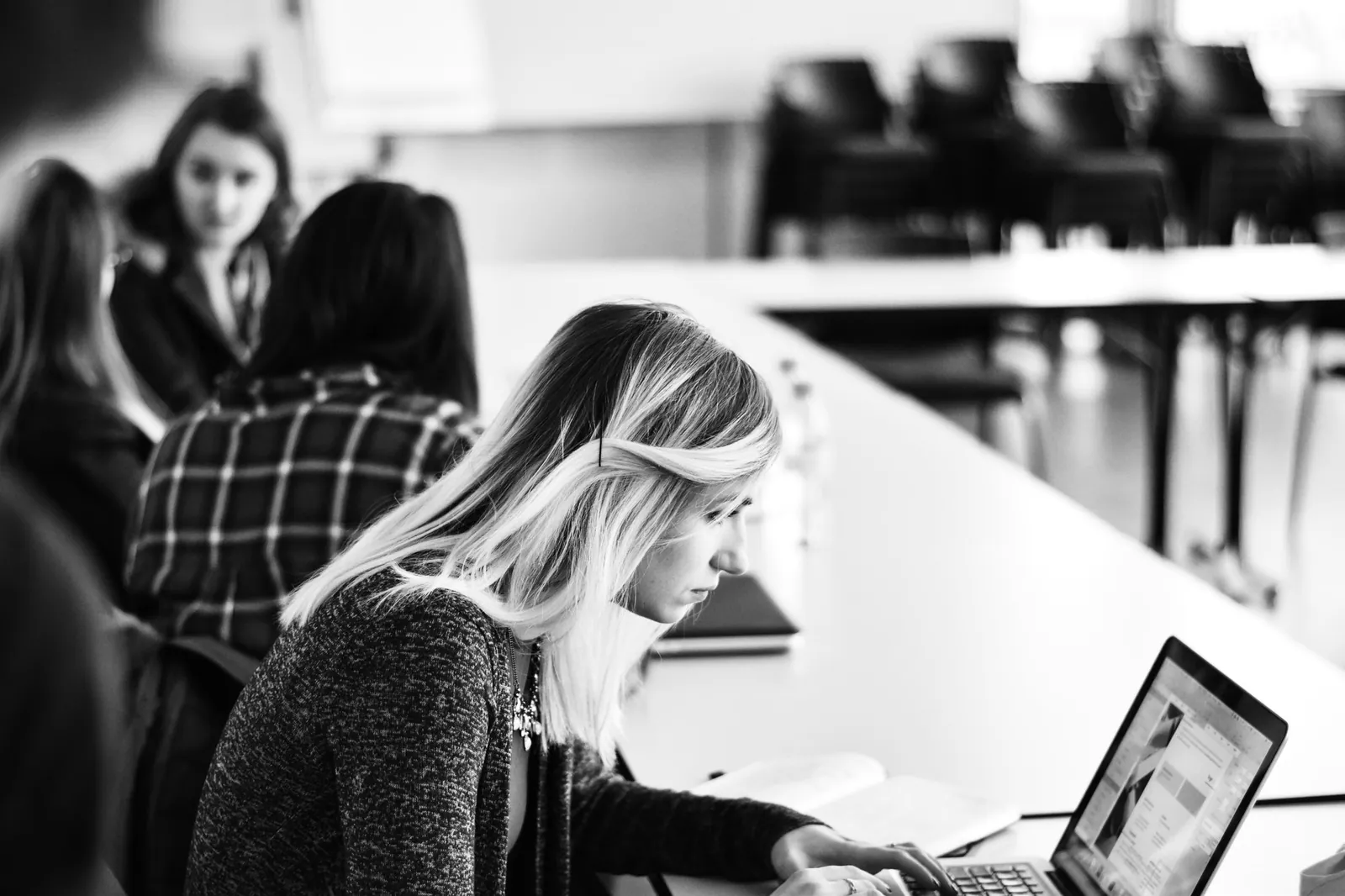 Students working together in a lecture room, one girl typing at a laptop