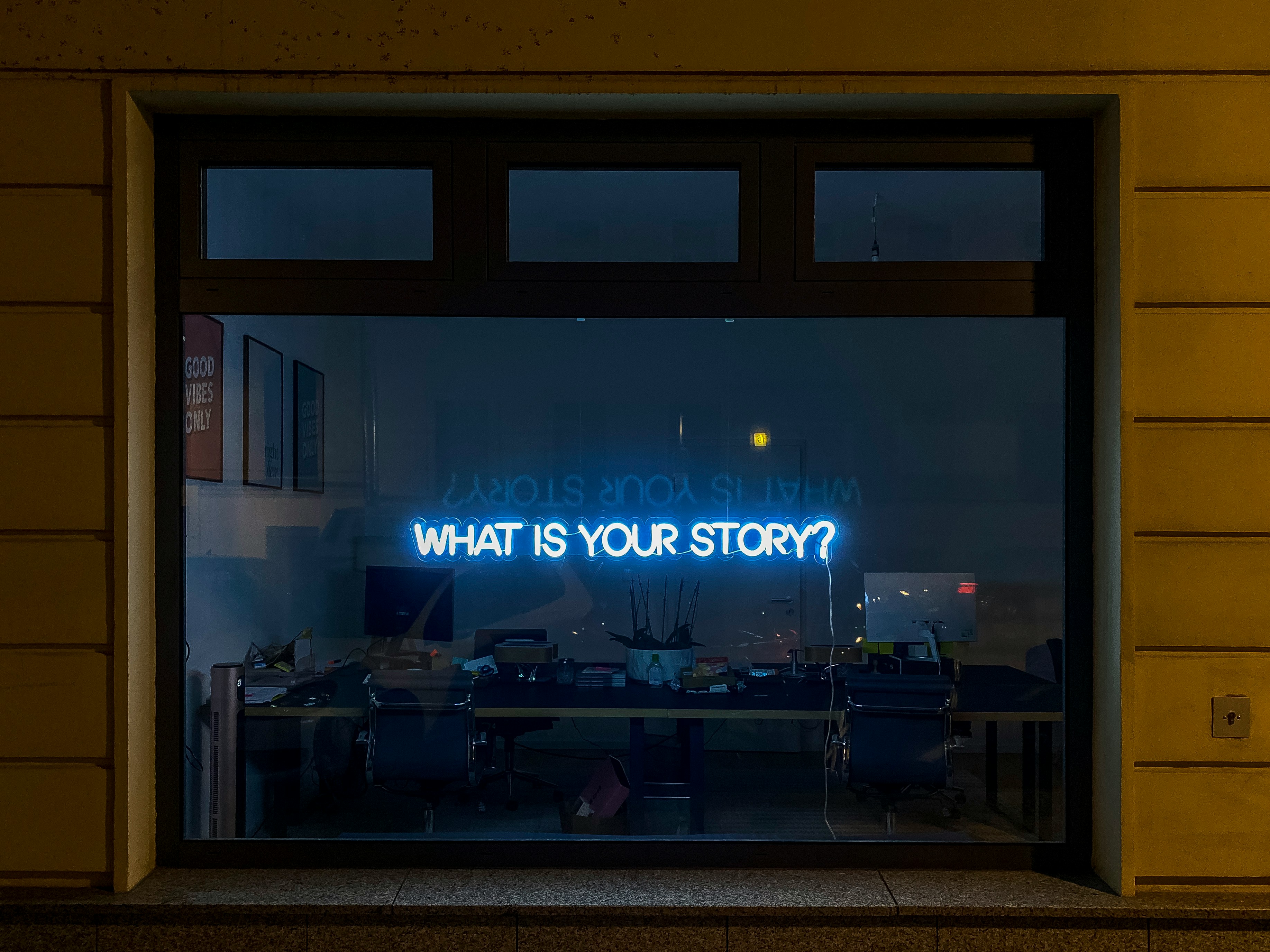 A shopfront window with a blue neon sign reading WHAT IS YOUR STORY?