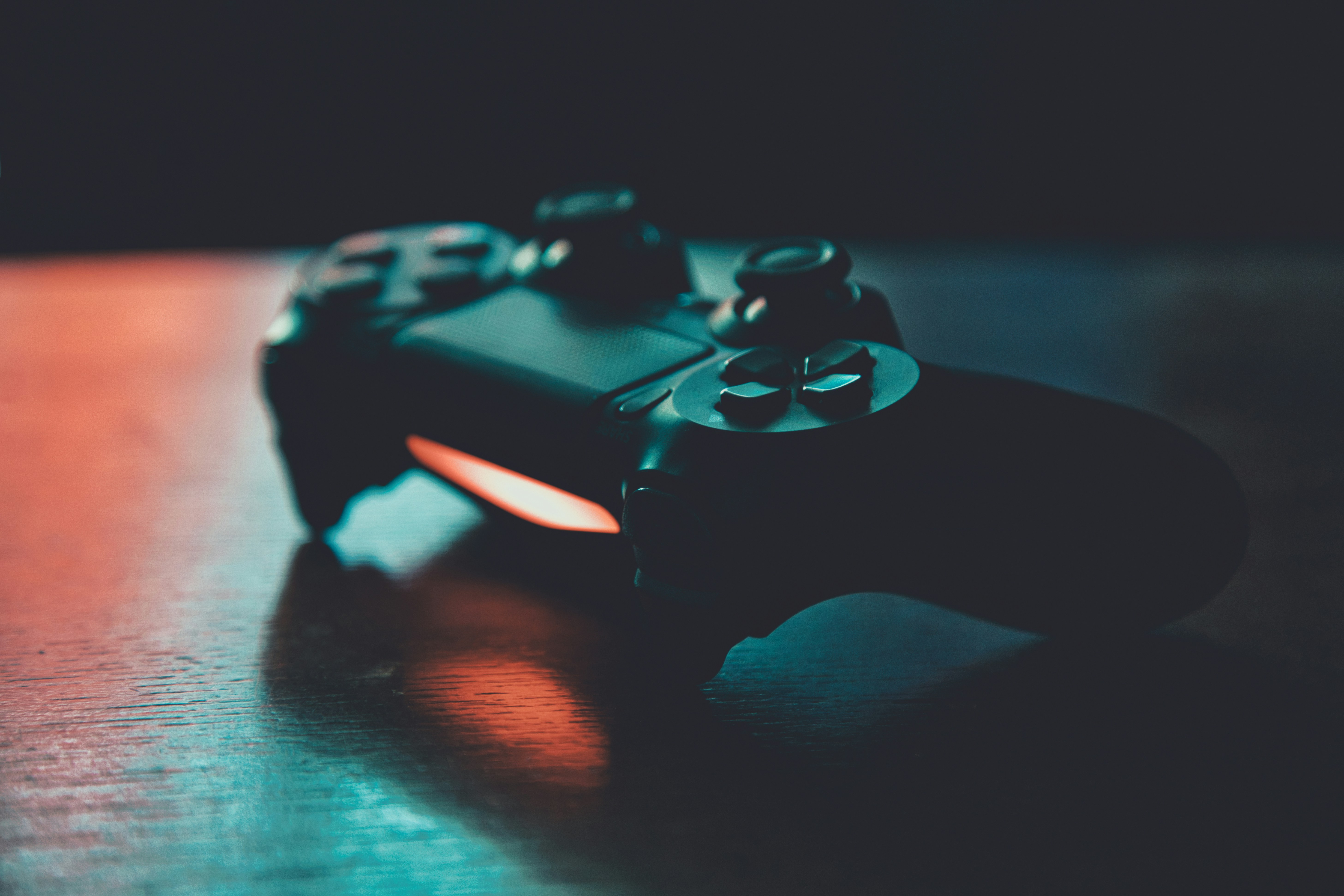 A games controller resting on a desk in a darkened room, screen light glowing behind it
