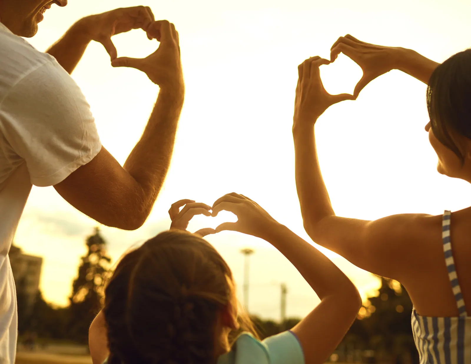 A family making heart shapes with their hands together in warm evening light