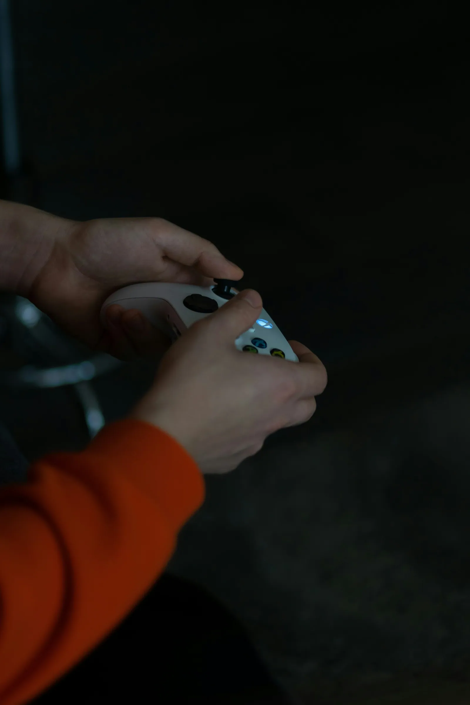 Close-up of hands holding a games controller in a dark room lit only by the screen