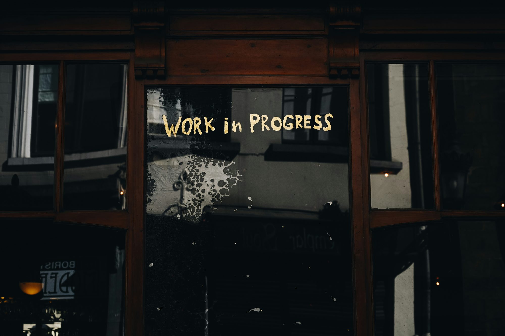 A hand-painted WORK IN PROGRESS sign in a darkened shop window