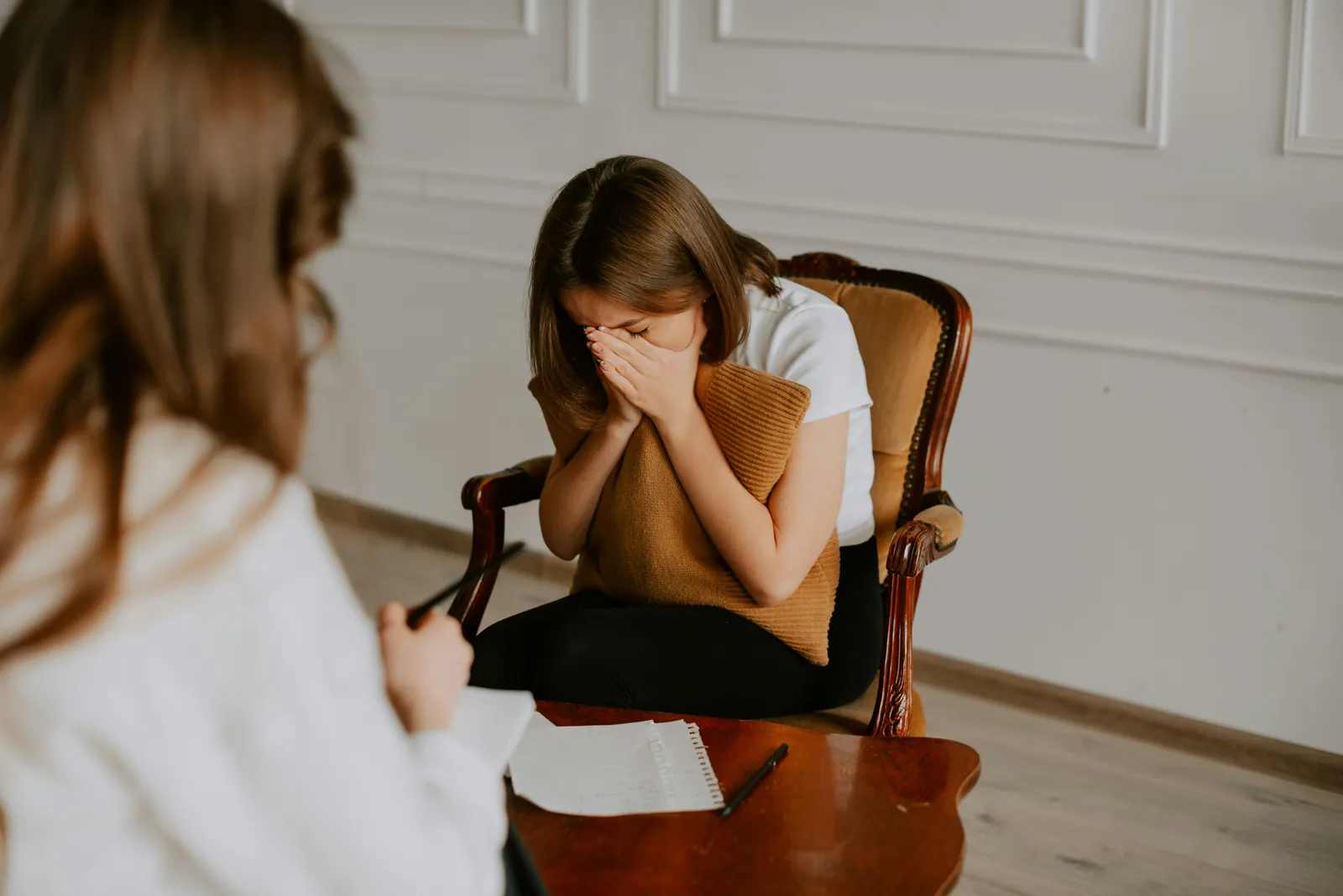 A teenage girl sitting in an armchair with her hands over her face during a counselling session
