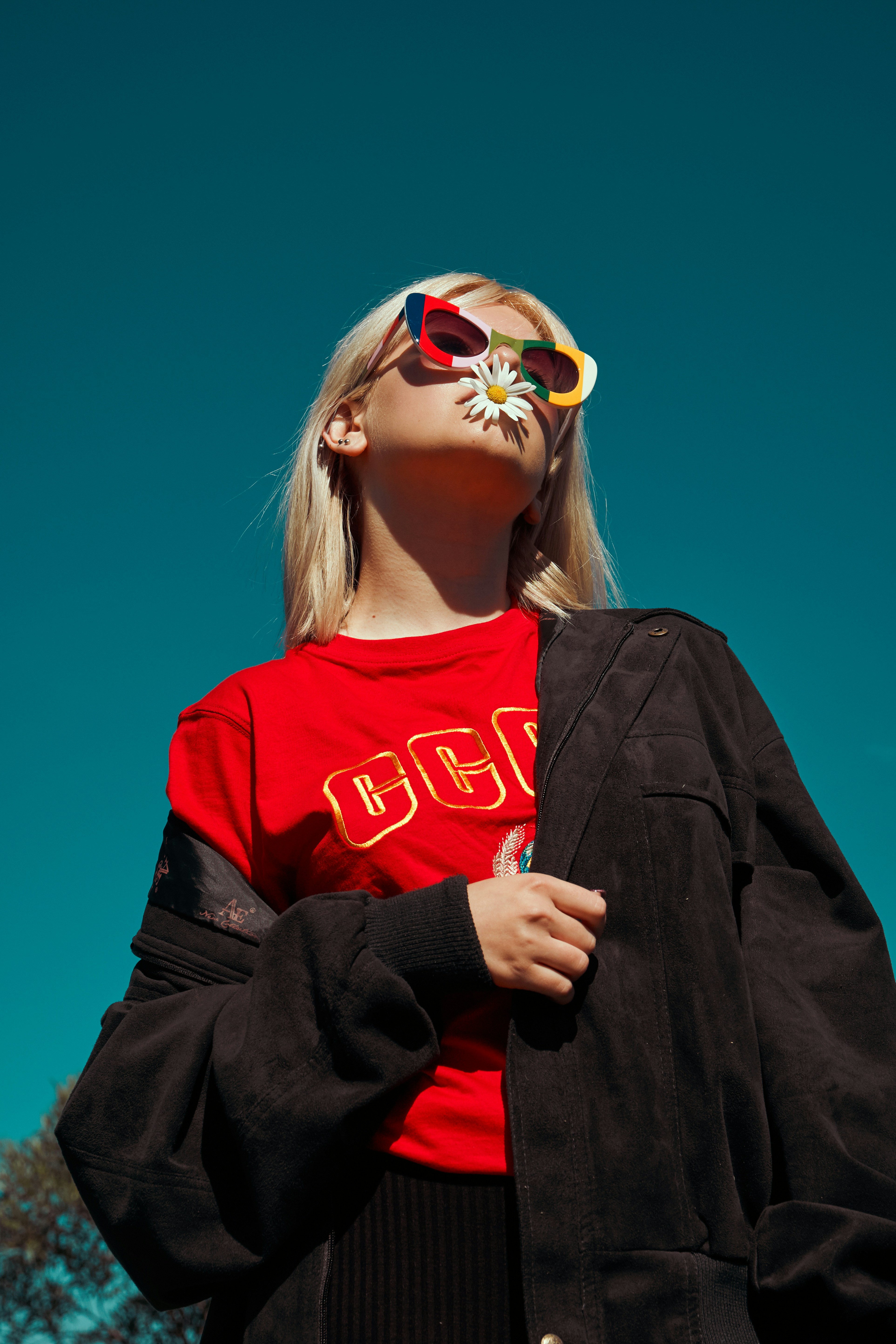 A teenager in bright sunglasses and a bold red top against a teal background