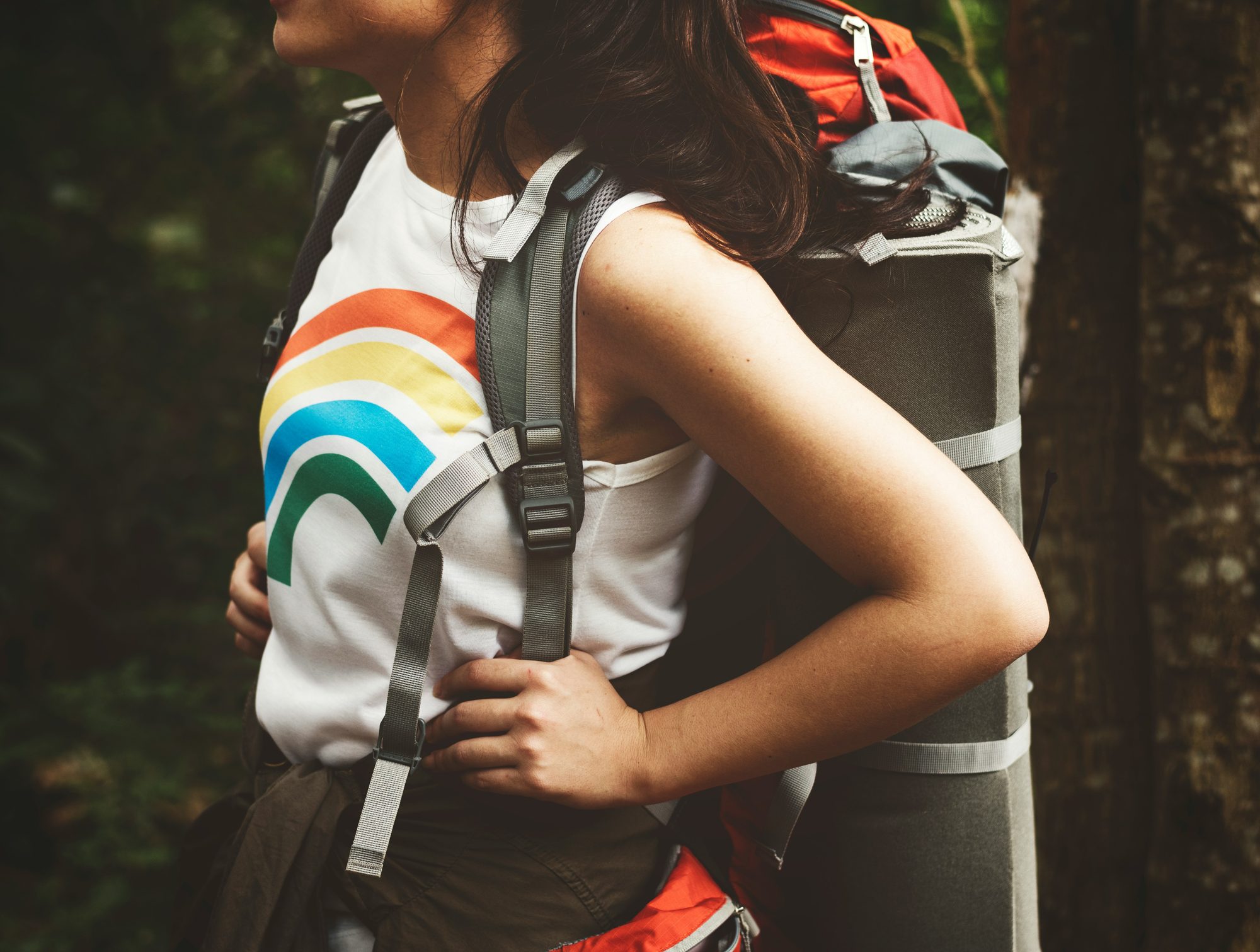 A teenager in a rainbow T-shirt shouldering a backpack outdoors