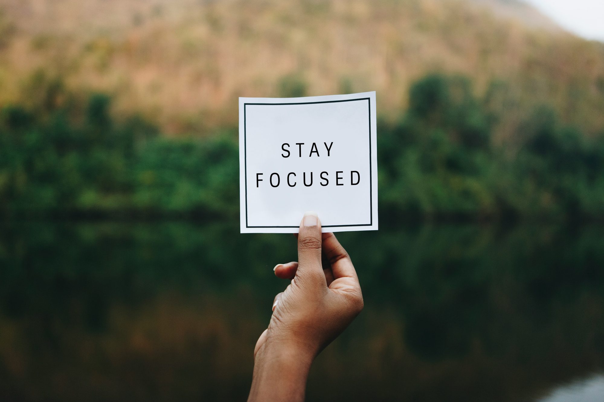 A small hand holding a card reading STAY FOCUSED in front of open water