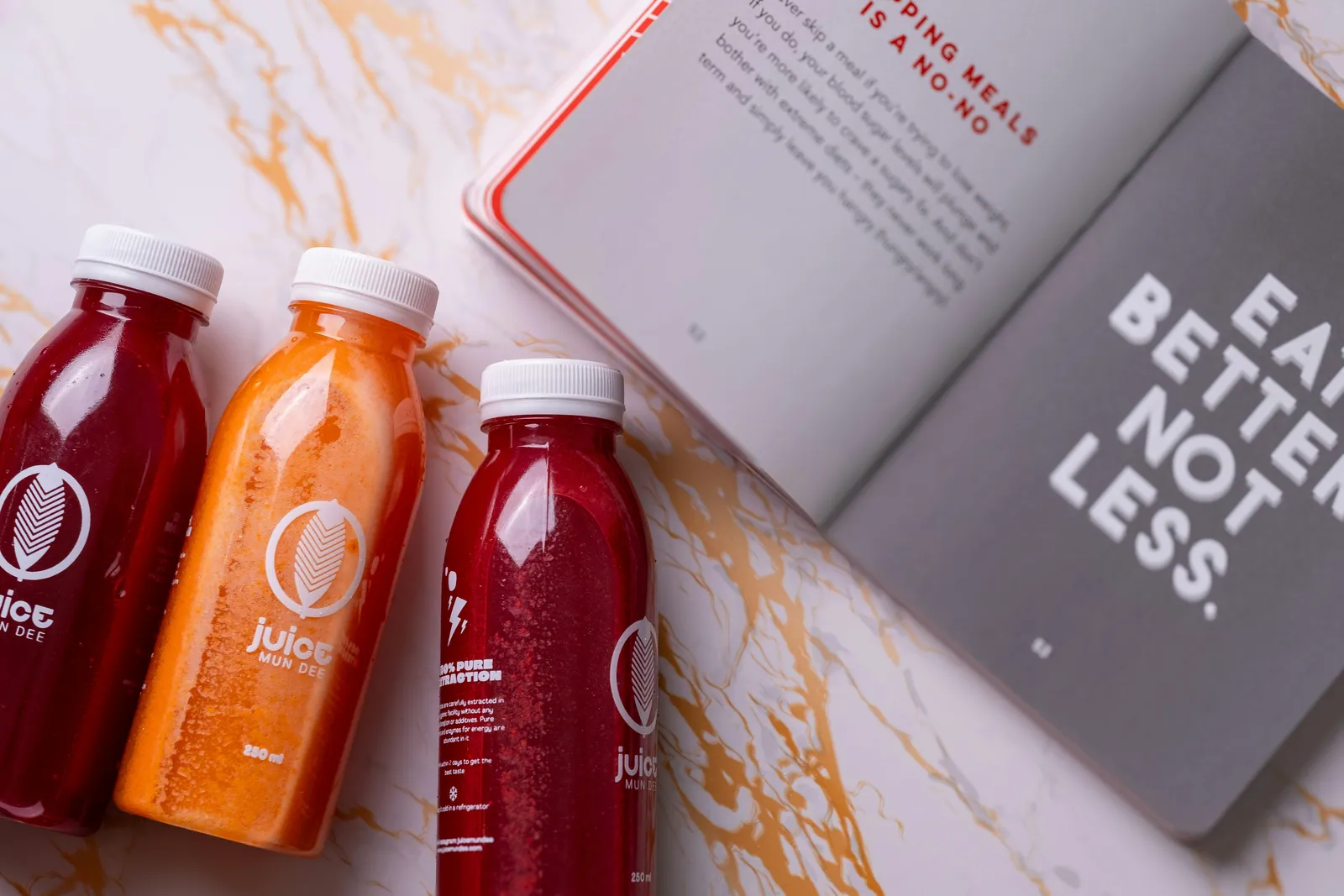 Bottles of brightly coloured juice beside an open book on a marble kitchen counter