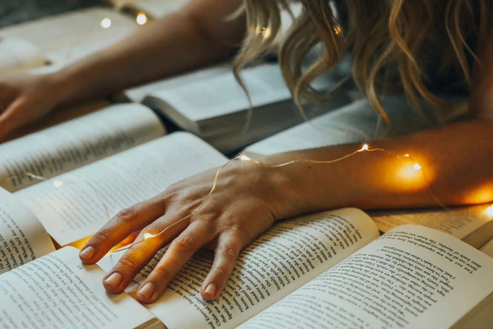 An open book under warm string lights on a desk late in the evening