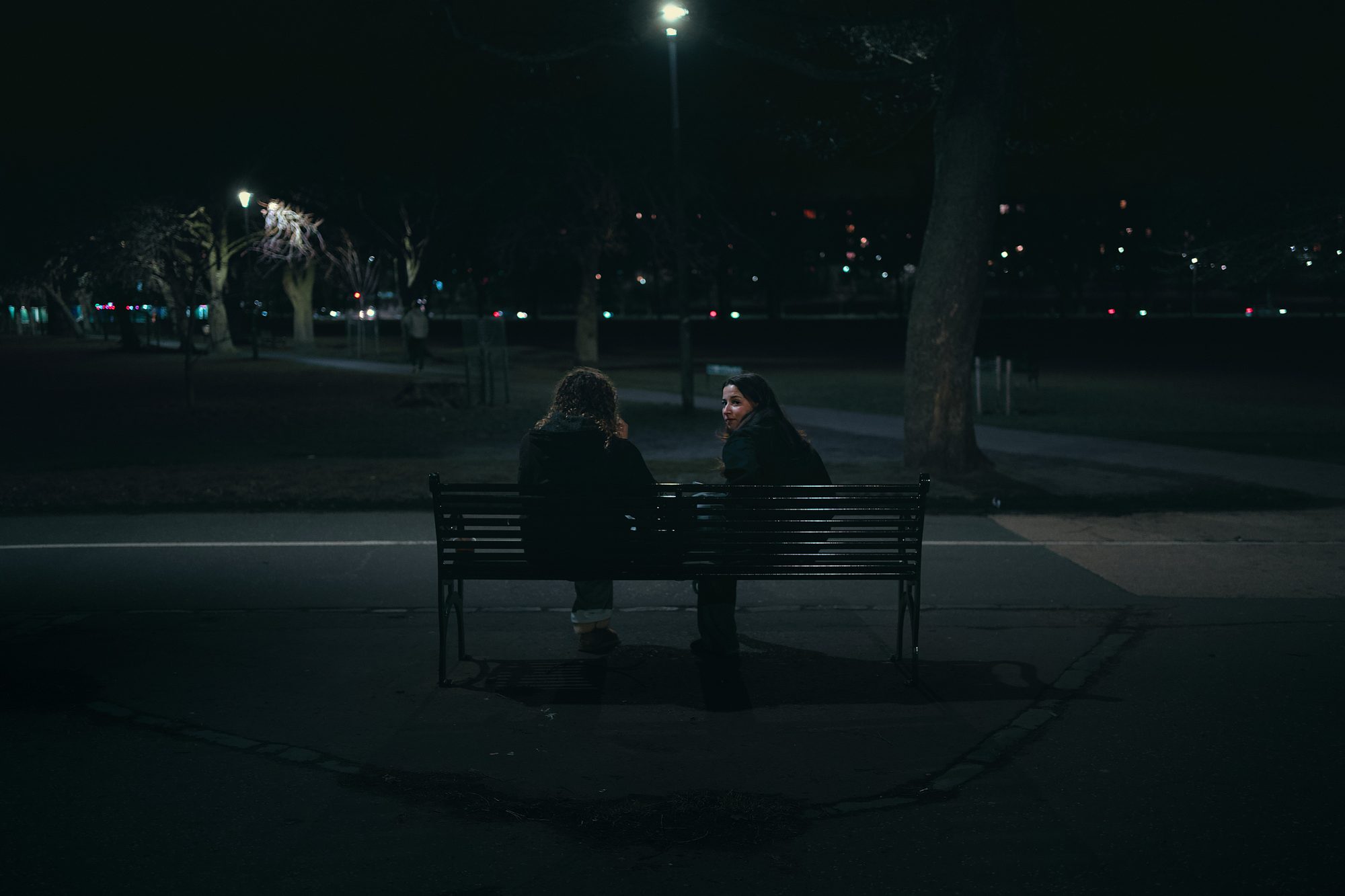 Two people sitting close together on a park bench at night