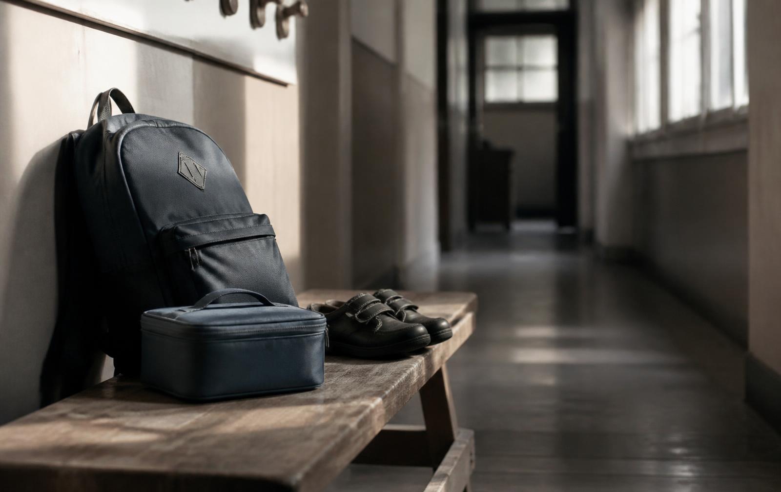 A 10-year-old child packing notebooks into a school bag at a kitchen table while a parent sits nearby