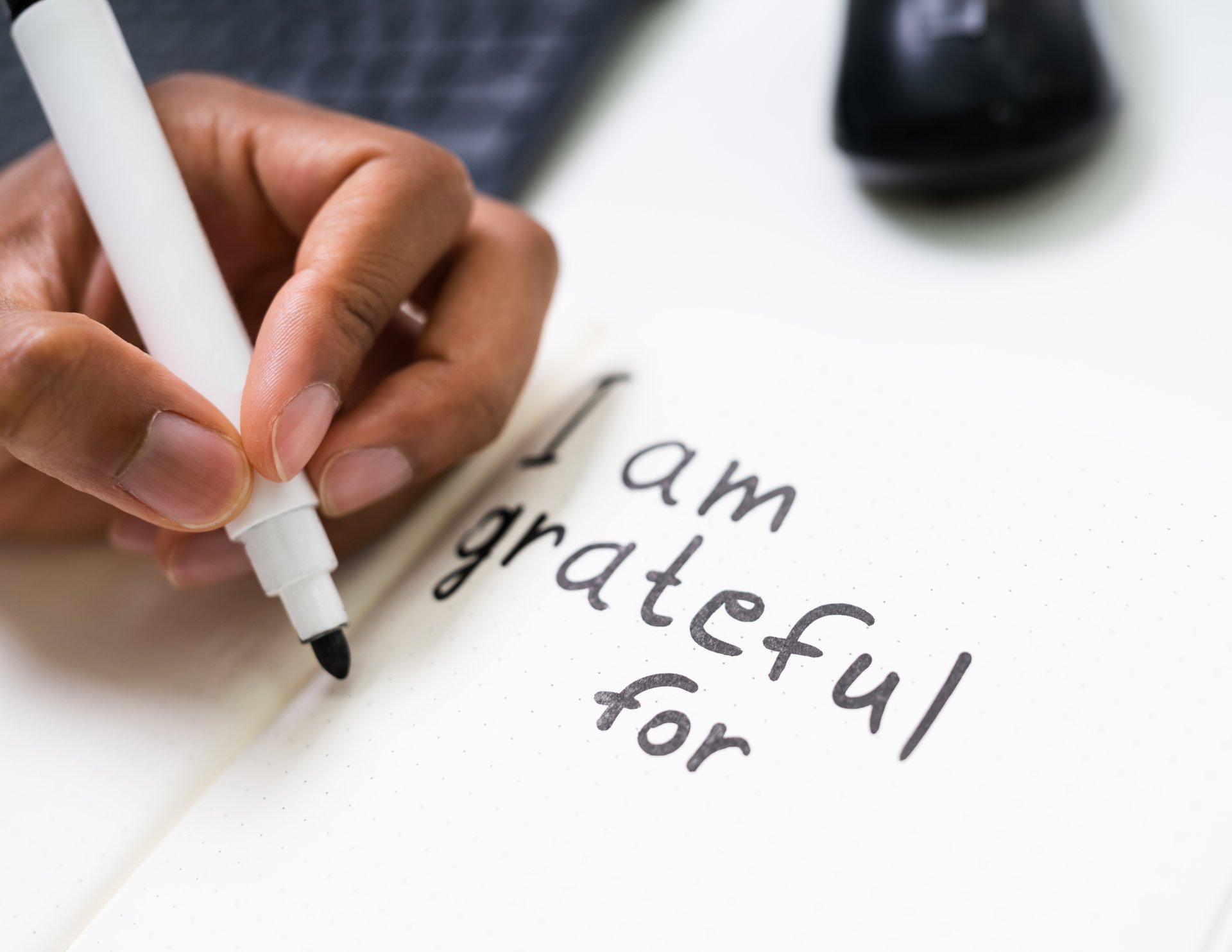 Hands writing a gratitude note: 'I am grateful for' on a sheet of paper