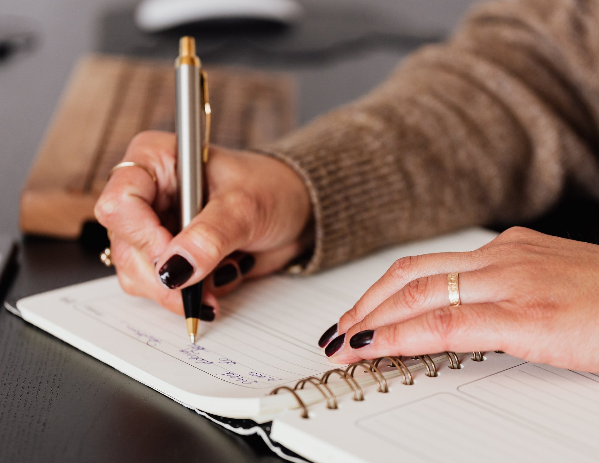 Hands writing lists and notes in a notebook on a quiet desk