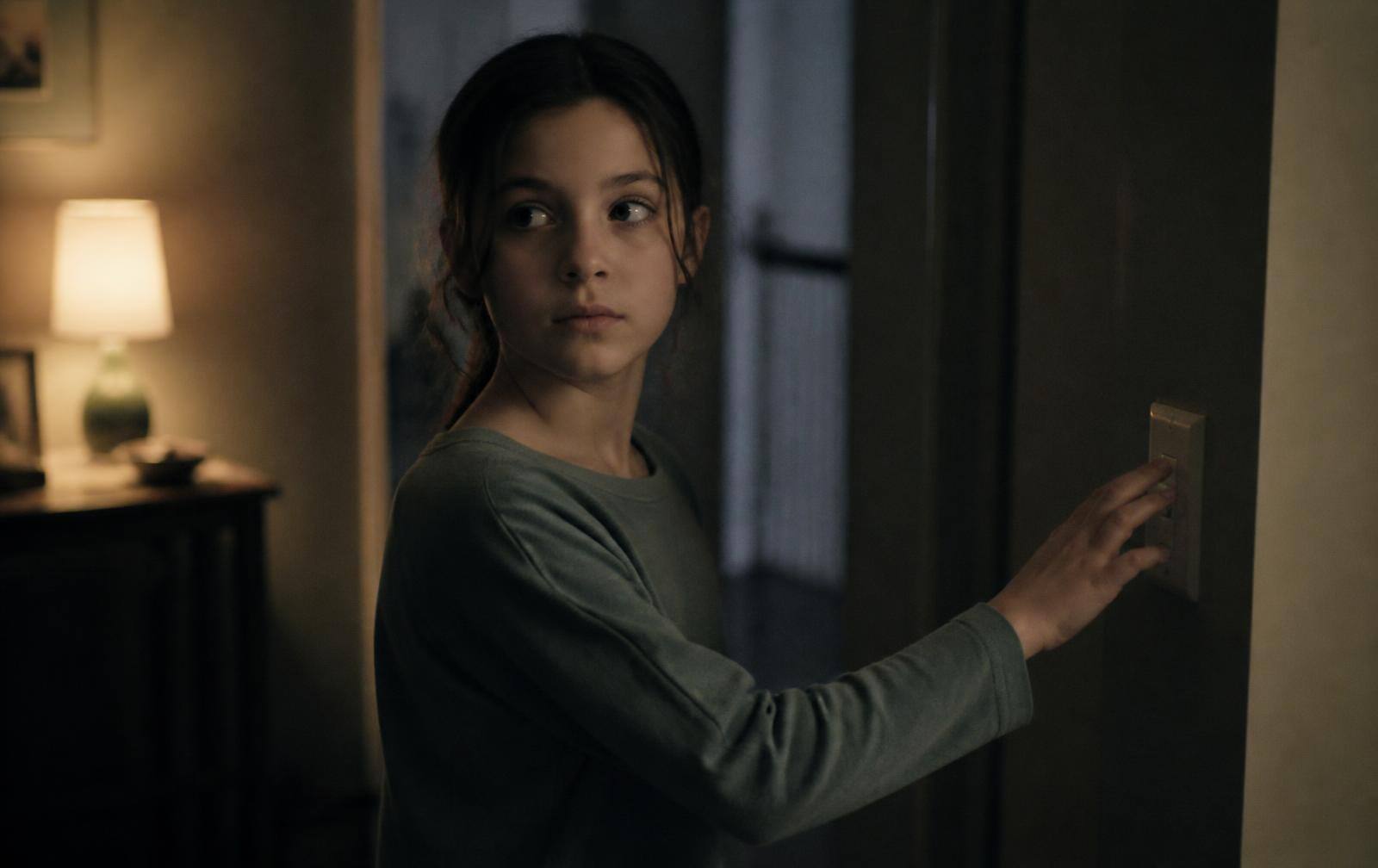 An eleven-year-old pausing in a dim hallway with a hand on the light switch, checking it again before bed