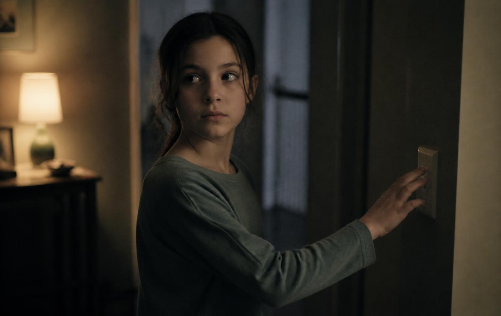An eleven-year-old pausing in a dim hallway with a hand on the light switch, checking it again before bed