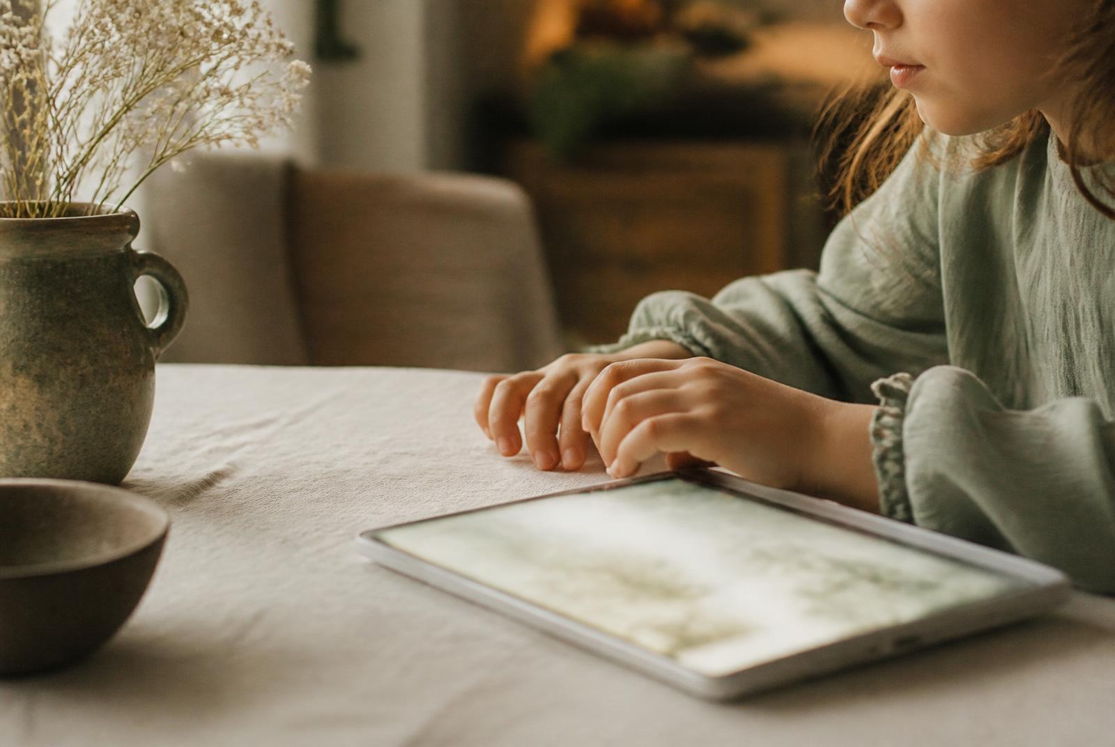 A child's hands resting beside a softly glowing tablet on a pale linen table
