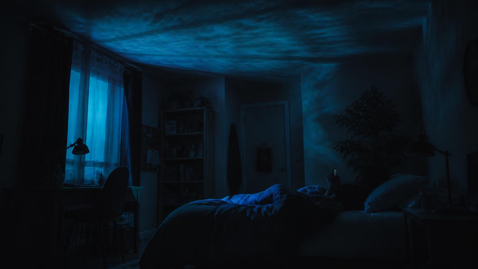 A darkened bedroom at night lit only by the blue glow of a phone screen