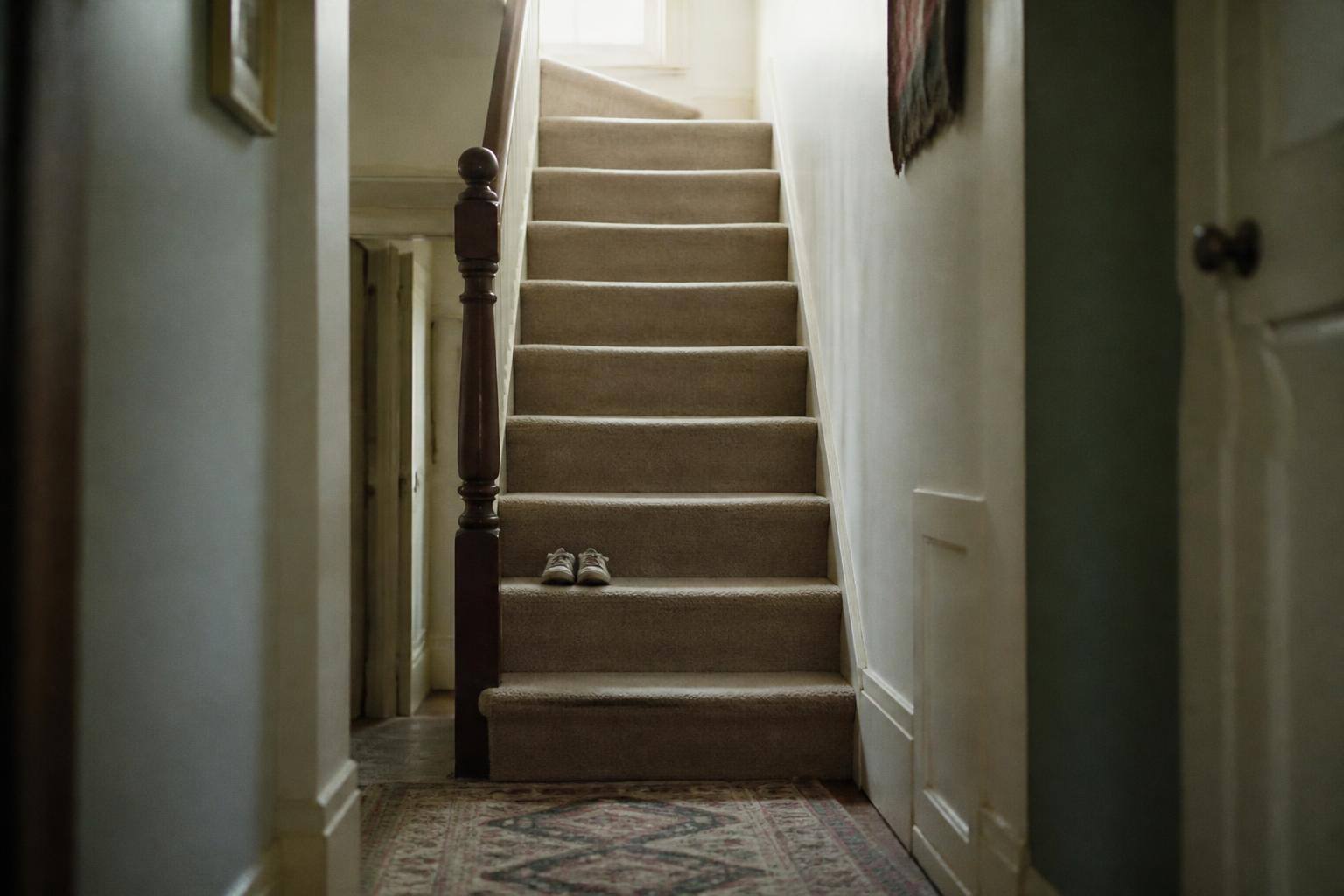A ten-year-old girl sitting on the stairs looking up at an out-of-focus adult, gentle indoor light