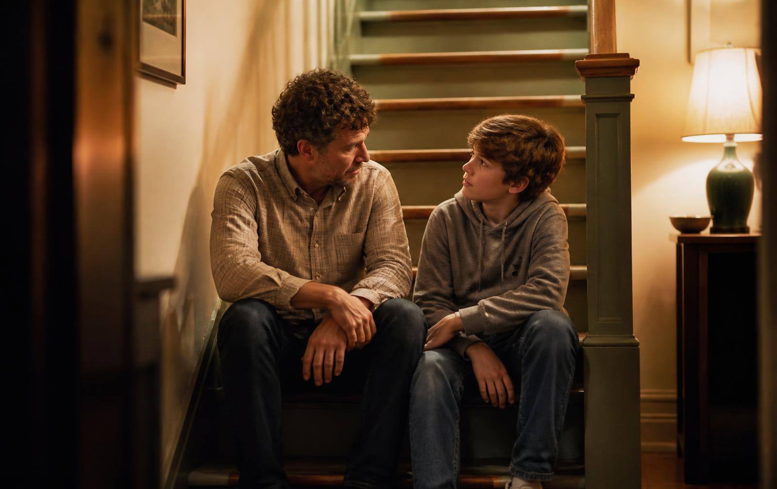 A parent and child sitting side by side on the bottom stair, talking quietly